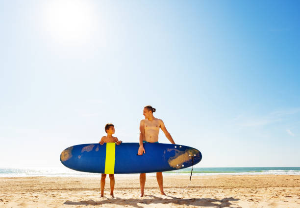 istock Father and son carry surf board on the sand beach 1211232314