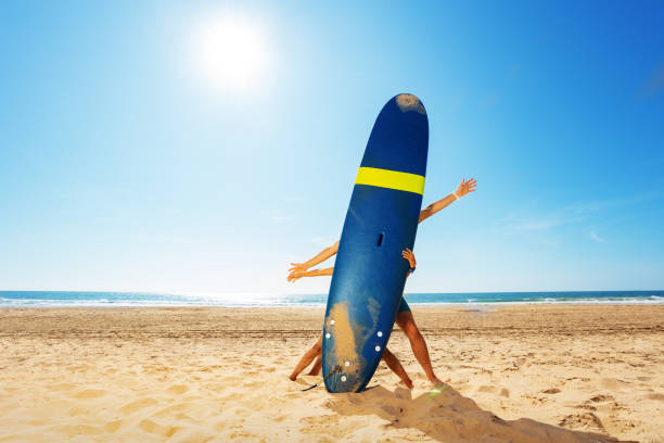 istock Child and adult behind surf board on a beach pose 1211232318