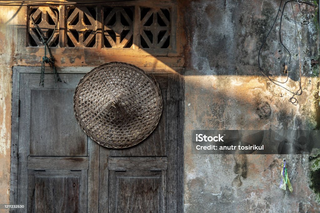 Chinese straw hat hung on the old wooden windows that are closed. Chinese straw hat hung on the old wooden windows that are closed. Selective focus. Agriculture Stock Photo