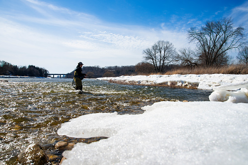Winter fishing for rainbow trout on a Great Lakes tributary.  A teen fisherman fly fishing on a beautiful bright winter day.