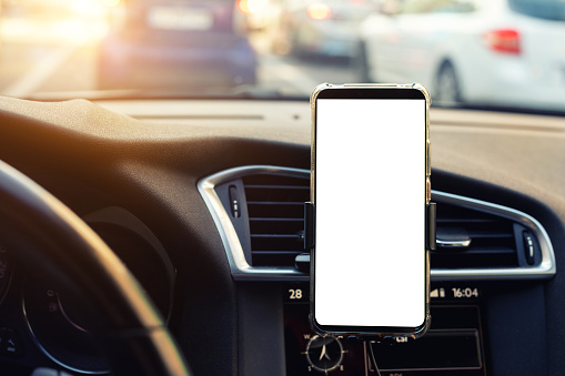 Modern smartphone device gadget mounted on phone holder at car dashboard. Mock-up white screen isolated template. Copyspace for text . Vehicle interior cockpit view. Traffic jam info app.