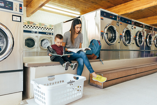 A mother and parent sits with her toddler son at a laundromat while studying for a university class. She is a hard working college student trying to earn her degree in education to improve her situation.