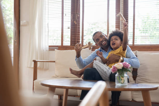 szczęśliwy afrykański ojciec i synek spędza czas grając drewnianą zabawkę samolotu w domu razem. - home interior arrival father family zdjęcia i obrazy z banku zdjęć