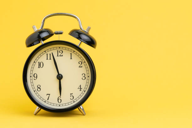 istock Alarm clock at almost 6 o'clock in the morning on yellow background with copy space using as business reminder, laziness or timer and deadline concept 1211255638