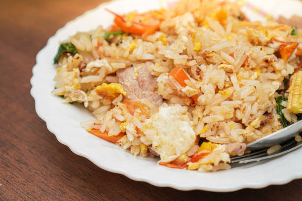 istock Close up and focus on fried rice mixed with various vegetables and meats in white plate place on dark brown wooden table 1211255749