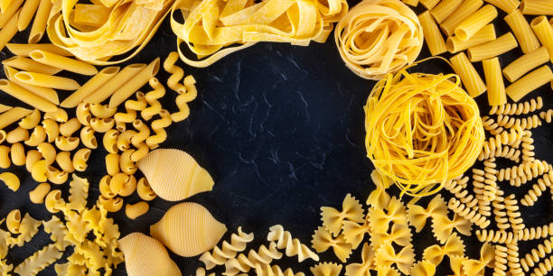 istock Italian pasta panorama with copy space, a flatlay of different pasta types, overhead shot on a black background with a place for text 1211268560