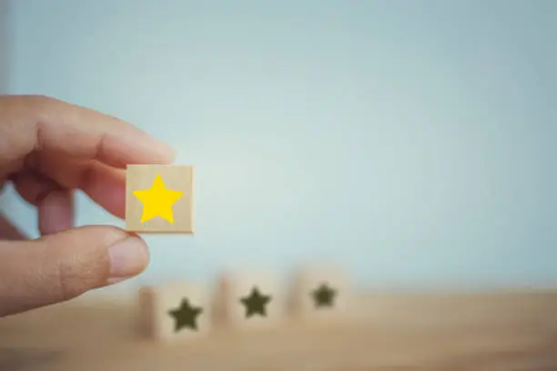 Photo of Business success: Hand chooses wooden yellow star shape on table. The best excellent business services rating customer experience concept.