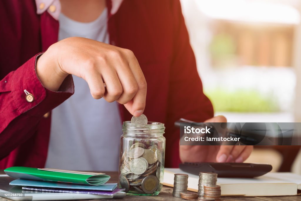 Saving money concept asian man hand putting coin write cost and Finance. expenses calculator, payments costs with paper notes, Financial and Installment payment concept. Saving concept Frugality Stock Photo