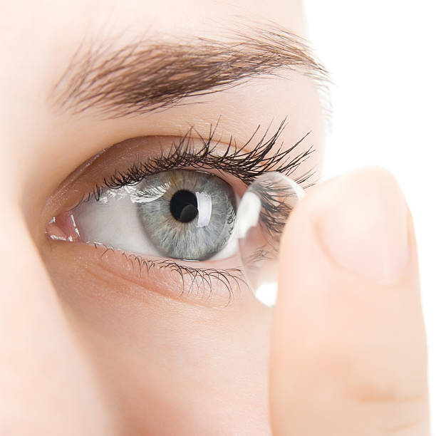 Woman putting contact lens into eye A young woman inserting a clear content lens into her left eye.  The woman's eye is blue, and she has brown eyebrows. lens eye stock pictures, royalty-free photos & images