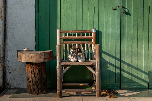 White canvas shoes put on a wooden chair to dry it at the front of the green wooden house door. Selective focus.