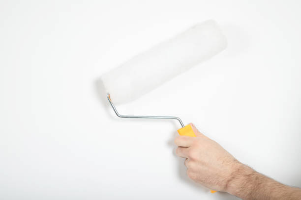 istock The guy holds a roller in his hand. White wall, repair. Builder 1211272217