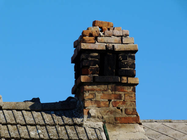 broken and grunge old brick meat smoker chimney broken and deteriorating grunge old brick meat smoker chimney. cracked mortar joints and loose bricks. clear blue sky. low angle view. weathered concrete tile sloped barn roof. black sooth deposit. sooth stock pictures, royalty-free photos & images