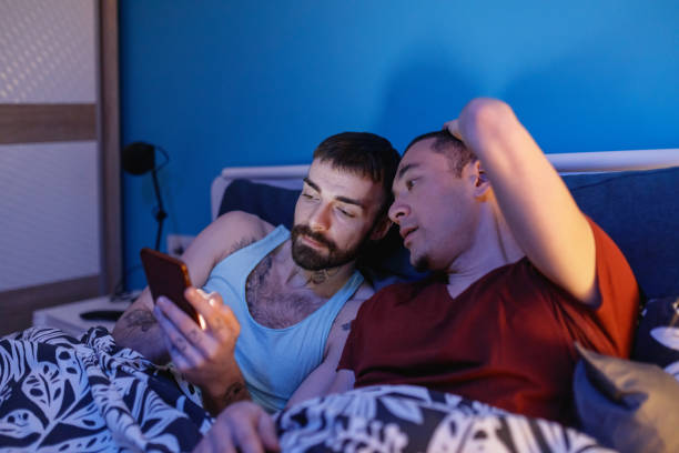 istock Gay couple watching content on mobile phone together in bed 1211282331