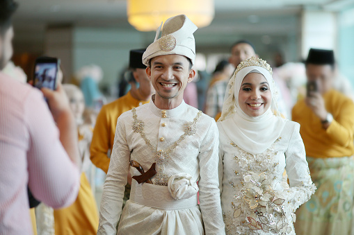 A pair of newlywed Muslim bride and groom holding hands walking into the reception hall in Kuala Lumpur, Malaysia.
