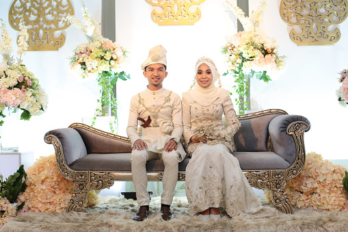 A pair of newlywed Muslim bride and groom seated at 'pelamin' (a decorated newlywed sitting at the main stage) in wedding reception, Kuala Lumpur Malaysia.