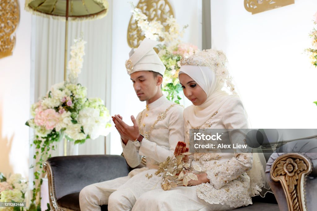 Modern Muslim Bride and Groom A pair of newlywed Muslim bride and groom seated for prayers at 'pelamin' (a decorated newlywed seating at the main stage) in wedding reception, Kuala Lumpur Malaysia. Wedding Stock Photo