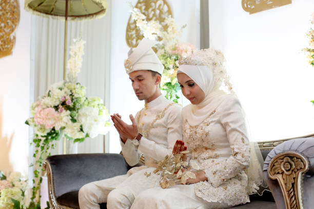 Modern Muslim Bride and Groom A pair of newlywed Muslim bride and groom seated for prayers at pelamin (a decorated newlywed seating at the main stage) in wedding reception, Kuala Lumpur Malaysia. asian wedding stock pictures, royalty-free photos & images