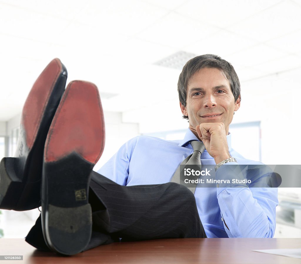 Uomo d'affari rilassanti con gambe sulla scrivania - Foto stock royalty-free di Adulto