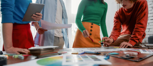 istock Latest design trends. Group of young designers in casual wear discussing ideas while working on a new project together in the modern and bright office. Creative agency 1211283735