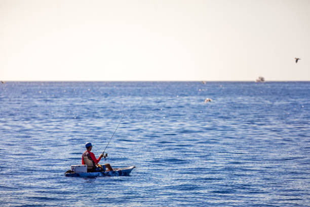 Los Christianos, Tenerife, Spain, February 1, 2020:  Man, fishing from a very small boat on the Atlantic Ocean