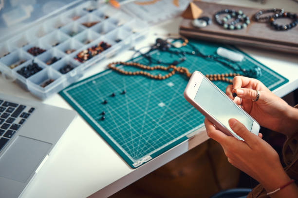 Girl is chatting by mobile phone Young woman is chatting by mobile phone while sitting next to table with her jewellery hobby. machine sewing white sewing item stock pictures, royalty-free photos & images