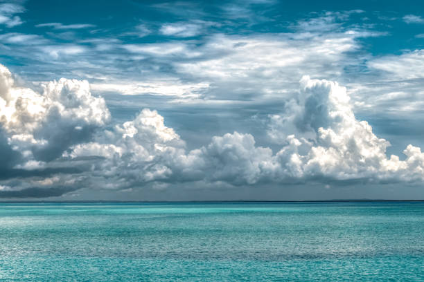 Calm ocean of turquoise color water and above it are huge dramatic cloud of type Cumulus during the onset of rainy season of monsoons; depicting the evaporation phase of Water cycle. Dream destination. Beautiful and breathtaking view of a seascape depicting the formation of clouds. The water is of turquoise color, the scene is free from any pollution. Concept of Water Cycle, Evaporation, Climate Change, Global Warming, Formation of Clouds, Scenery, Calm, Relaxation, Island, Vacation etc. el nino stock pictures, royalty-free photos & images