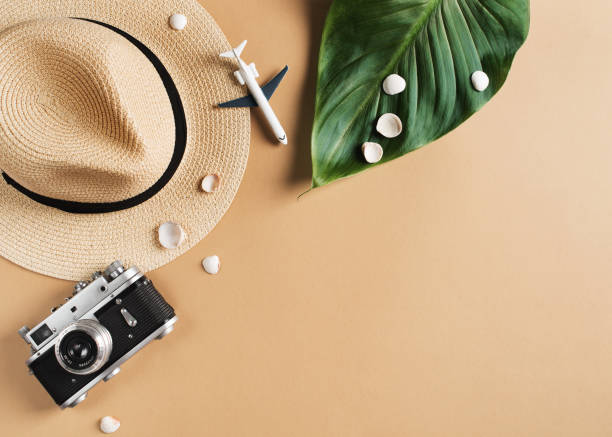 istock Vacation flat lay frame with hut, laeves camera and other accessories on beige background 1211291223