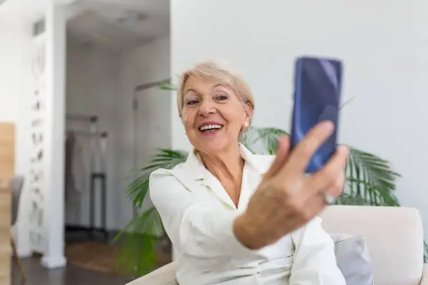 Grandma Taking Selfies at Home in the Livingroom. Close Up Portrait of Happy Cheerful Delightful Charming Beautiful Elderly Lady Granny Grandma Taking a Selfie. Old-Age, Retirement and People Concept