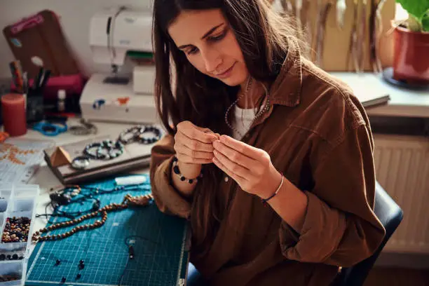 Happy smiling woman is working on beads jewellery at her own workplace.