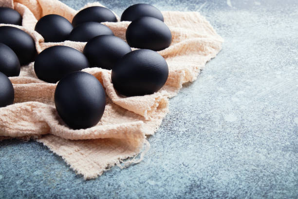 istock Black Easter eggs on a linen napkin on a blue texture table. Easter celebration concept. 1211294645