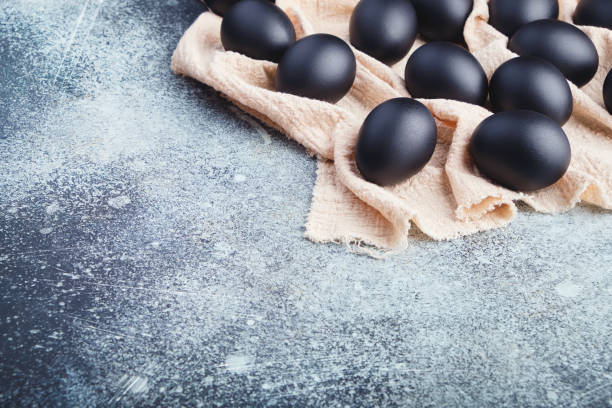 istock Black Easter eggs on a linen napkin on a blue texture table. Easter celebration concept. Copy space 1211294674