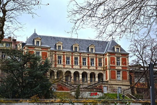 Saint-Etienne, France - January 27th 2020 : Focus on a large building made of red bricks and stones, located on one of the hills of the city.