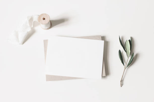 istock Summer wedding stationery mock-up scene. Blank horizontal greeting card, envelope, ribbon and olive branches isolated on white table background. Feminine Mediterranean flat lay, top view. 1211298156