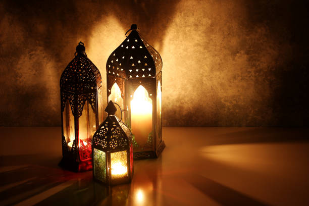 istock Ornamental Arabic lanterns with burning candles on table glowing at night. Festive greeting card, invitation for Muslim holy month Ramadan Kareem. Iftar dinner background with golden glow. 1211298240