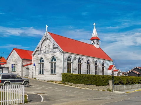 A quaint, old-fashioned wooden church, built in 1899, with white peeling paint and a red roof, steeple and cross, and a vibrant blue sky with wispy clouds in the background. Copy space.