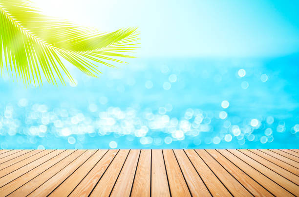 istock Blur tropical beach with bokeh sun light wave and palm tree on copy space empty old wood table abstract background. 1211309742