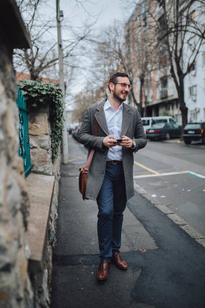 istock Man using mobile phone while walking on street to office 1211310669