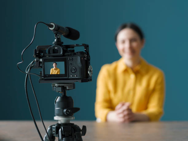 Professional vlogger sitting in front of a camera Smiling woman sitting in front of a camera and making a video blog multimedia studio stock pictures, royalty-free photos & images
