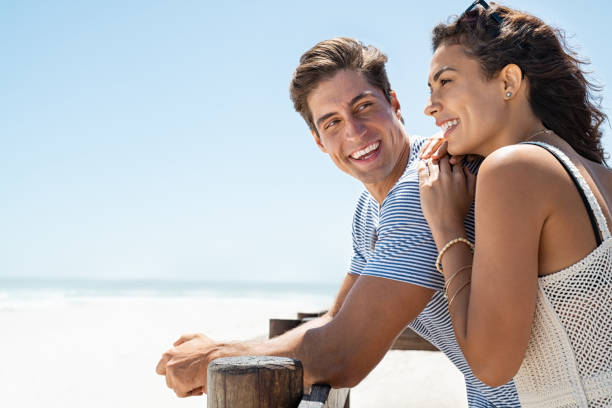 pareja sonriente disfrutando del día en la playa - leaning forward fotografías e imágenes de stock