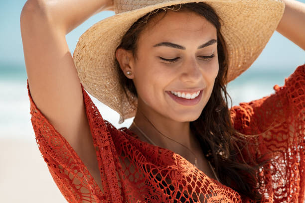 Glamour girl wearing straw hat at beach Carefree young woman at beach enjoying summer holiday. Portrait of happy smiling hispanic woman relaxing at sea during vacation. Close up face of beautiful fashion girl with red crochet dress walking on the beach. straw hat photos stock pictures, royalty-free photos & images