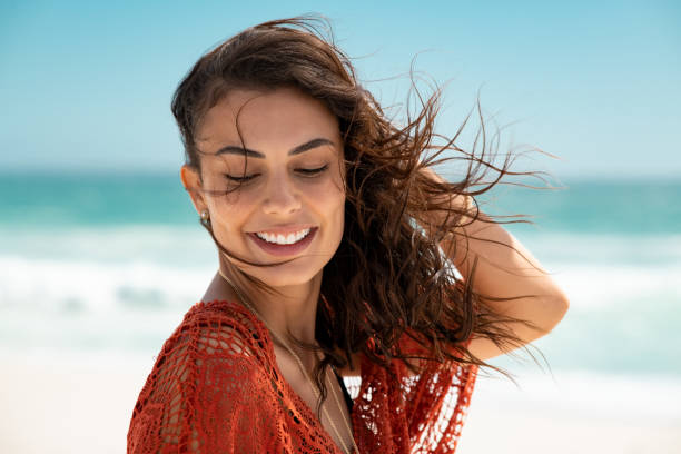 Beautiful latin woman enjoying wind at beach Latin fashion woman wearing red lace dress at beach and enjoy fresh breeze. Portrait of carefree tanned girl relaxing at beach during summer vacation. Young smiling beauty woman during summer vacation. beach hair stock pictures, royalty-free photos & images