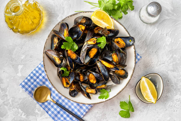 istock Cooked mussels in a white plate with parsley and lemon on light background 1211319616