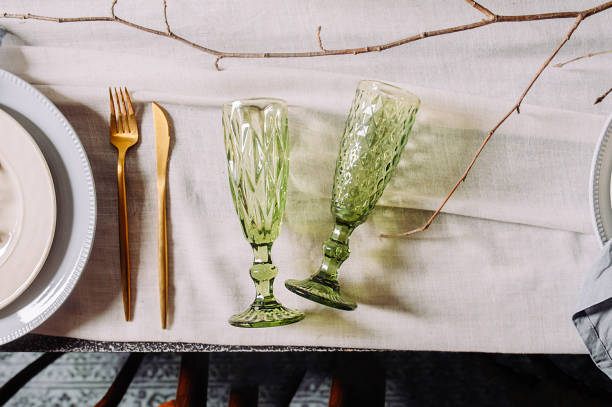 istock Two empty green vintage shaped drink glasses on a cotton old tablecloth, top view, hard light. Table setting in a mysterious spring style with live plants and branches. 1211320080