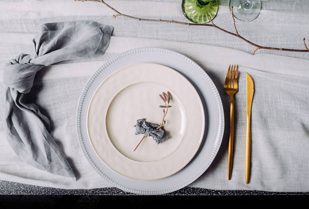 istock Eco-friendly natural table setting. Two white vintage plates with a gold fork and a gold knife and a cotton blue-gray napkin on a white vintage tablecloth, top view. 1211320272