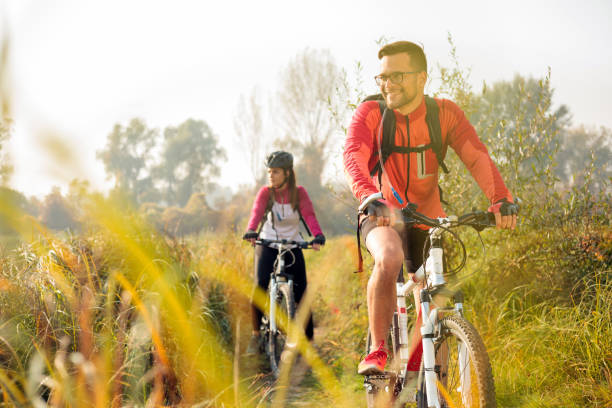 feliz joven pareja montando bicicletas de montaña a lo largo del sendero - riding autumn meadow land fotografías e imágenes de stock