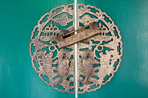 Stock photo showing a fish shaped, metal padlock covered in rust and verdigris, and an ornate key hanging on nail in red wooden board.