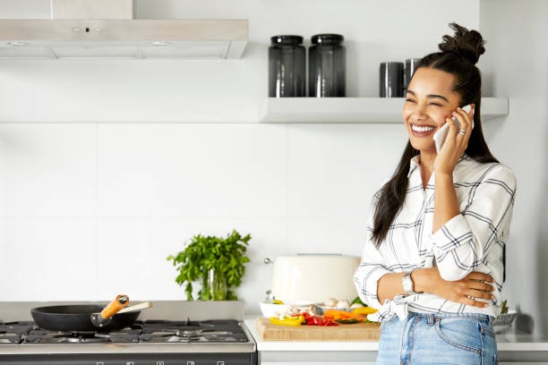 istock Smiling woman talking on smart phone in kitchen 1211322015