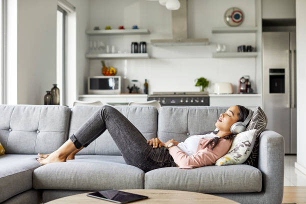 femme appréciant la musique tout en se reposant sur le sofa à la maison - lying on side audio photos et images de collection