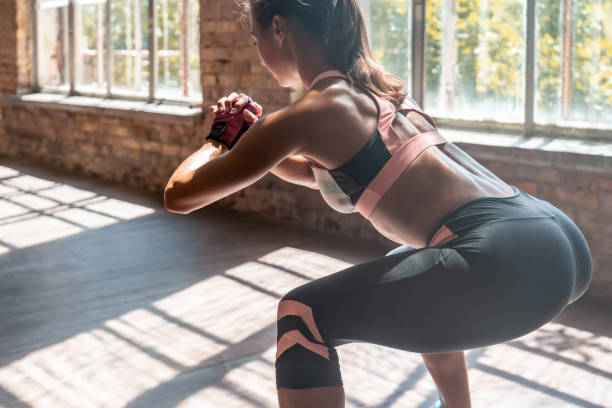 closeup jovem sporty mulher treinadora de fitness fazer agachamentos de peso corporal praticar exercício de agachamento com as mãos entrelaçadas curvando-se para a frente manter a forma em moderno chão de madeira de academia estilo de vida saudável es - crouching - fotografias e filmes do acervo