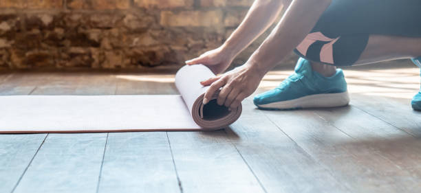 クローズアップハンドアクティブスポーティな女性ローリング折りたたみ式折りたたみベージュスポーツフォームゴムマットは、練習ヨガトレーニングは、現代のジムフィットネススタジオ� - stretching yoga exercise mat women ストックフォトと画像